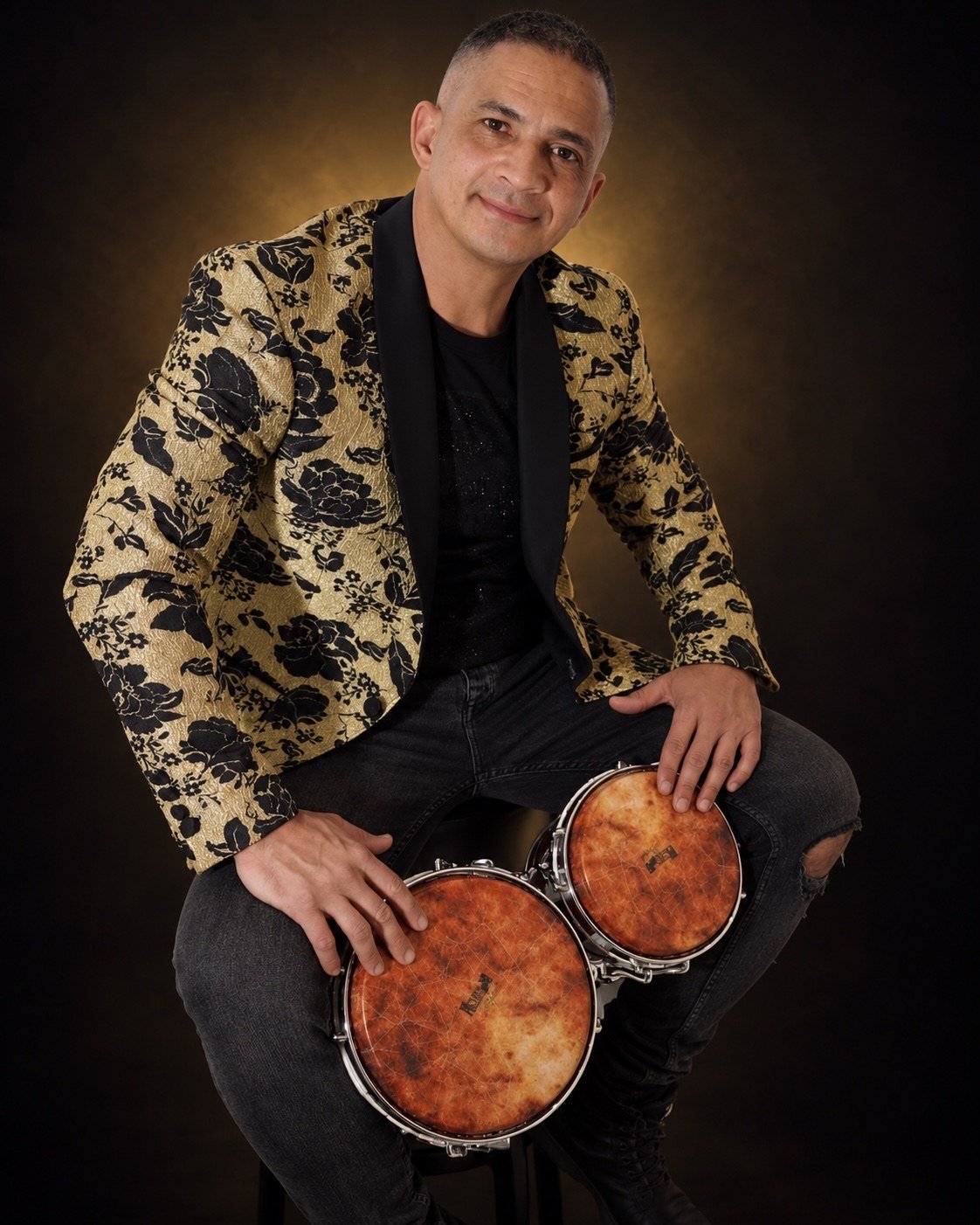 Arlexis Ayala, director artístico de La Xclusiva Salsa, sentado con sus bongós